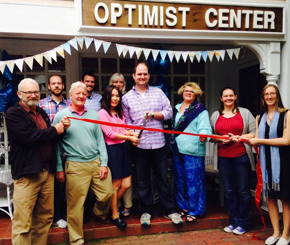 A group cutting a red ribbon under the Optimist Center sign and bunting