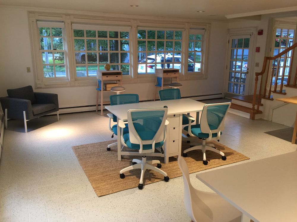 The finished idea room: bright white walls, coworking tables with teal chairs, and armchairs