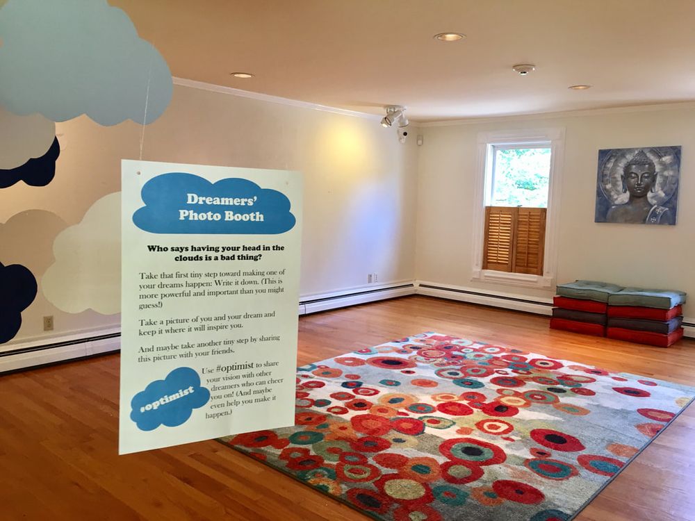 A Dreamers’ Photo Booth sign on a colorful rug, with painted clouds on the wall