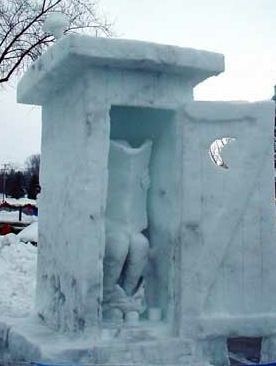A snow sculpture of an outhouse with a crescent moon cut into its door, a snow figure seated inside with a newspaper