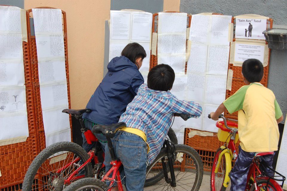 Children lean over their bikes to read the handwritten essays pinned up on display boards