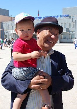A smiling father in a hat holds his young son in the town square