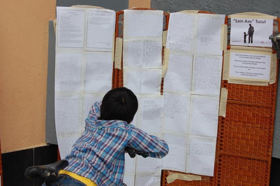A boy reads the essays pinned to a display board beside a small Sain Aav Tosol sign